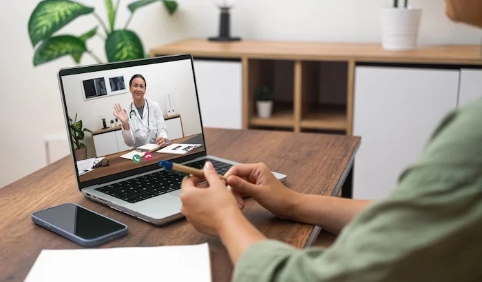 Person having a telehealth virtual medical consultation on a laptop, speaking with a doctor on a video call.